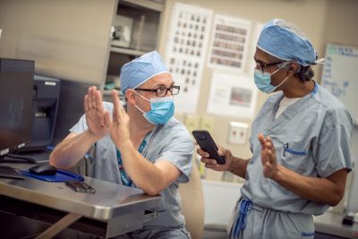 Two healthcare professionals in scrubs and masks at a computer.