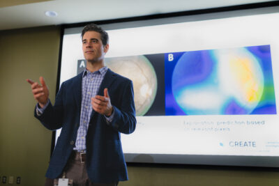 Photo of Dr. Jeremy Petch, behind a large screen showing an abstract image from the CREATE team